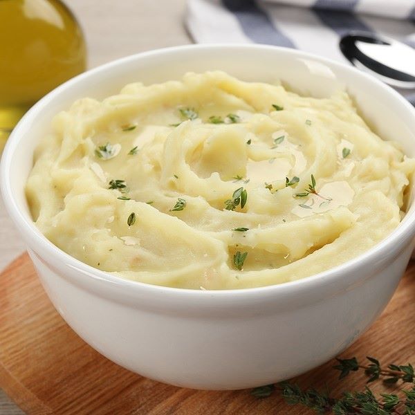 Creamy mashed potatoes garnished with herbs and served in a white bowl.
