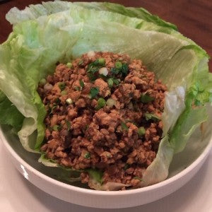 Seasoned ground chicken and chopped green onions served in crisp lettuce leaves in a white bowl.