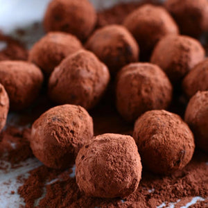 Chocolate covered cherries truffles coated in cocoa powder and arranged on a dusting of cocoa.