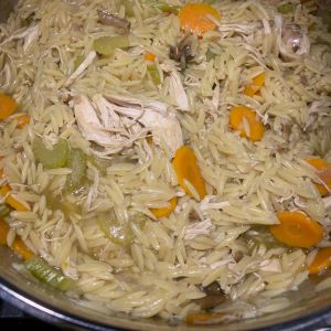 A bowl of orzo pasta with sliced celery, carrots, and mushrooms.