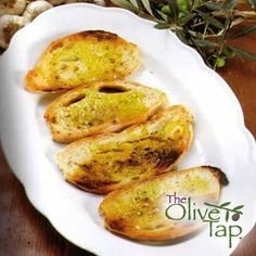 Four toasted baguette slices drizzled with olive oil on a white plate.