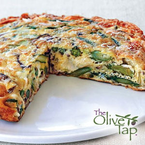 An asparagus and porcini mushroom olive oil frittata on a white plate with a slice missing and The Olive Tap logo in the righthand bottom corner.
