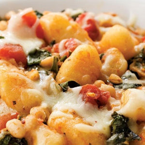 A close-up of gnocchi with spinach, cannellini beans, diced tomatoes, and melted cheese.