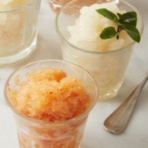 Two glasses of fruit granita with a frozen texture, one garnished with fresh mint leaves and served on a white surface.