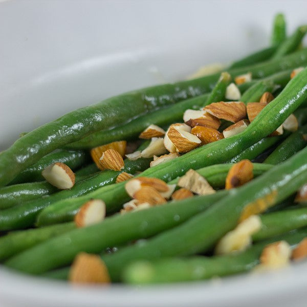 Green beans topped with sliced almonds served in a white bowl.