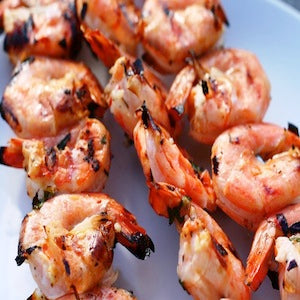 Three skewers of grilled shrimp served on a white plate.