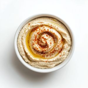 Creamy roasted garlic hummus drizzled with olive oil and sprinkled with paprika in a white bowl on a white surface.