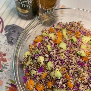 A quinoa salad with diced cucumber, red cabbage, red onion, and orange cherry tomatoes served in a glass bowl.