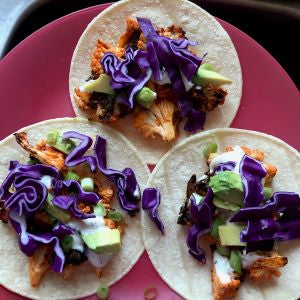 Tortillas topped with buffalo cauliflower, shredded purple cabbage, and avocado, served on a pink plate.