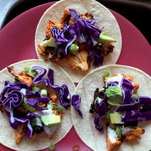 Tortillas topped with buffalo cauliflower, shredded purple cabbage, and avocado, served on a pink plate.