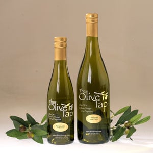 Two bottles of The Olive Tap olive oil displayed with olive branches against a neutral background.