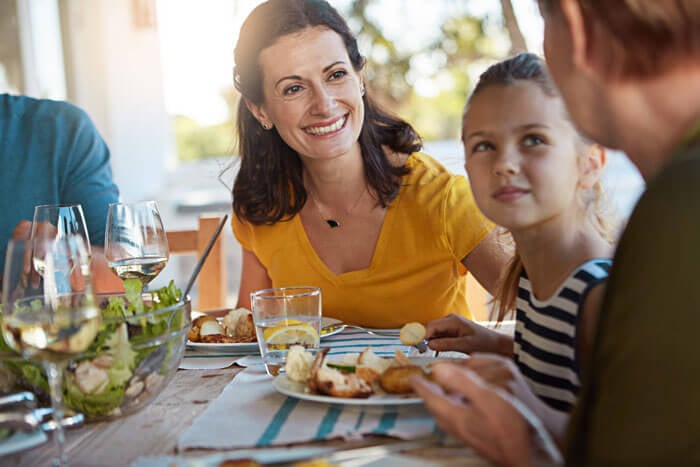 A child with a man and woman seated at a dinner table with a plate of food.
