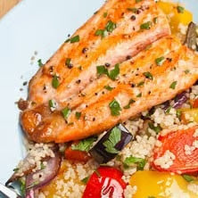 Salmon fillet seasoned with herbs and spices, served over a colorful couscous salad with roasted vegetables, olives, and fresh herbs.