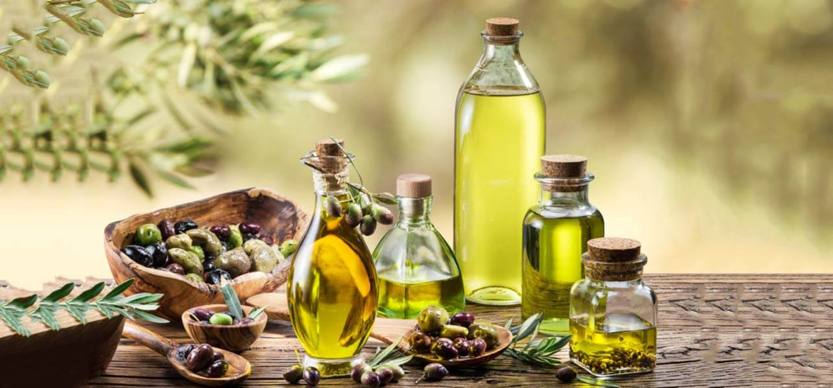 Glass bottles of olive oil arranged on an outside table with olive branches and olives in bowls.