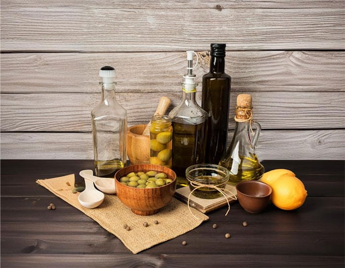 A collection of olive oil bottles, olives, and lemons arranged on a table with wooden bowls and serving pieces.