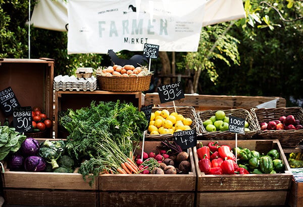 Wooden crates of vegetables such as carrots, radishes, peppers, beets, lemons, and limes at a farmer's market.