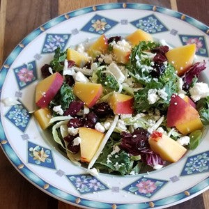 Kale salad mix topped with peaches and feta cheese crumbles, served on a decorative plate.