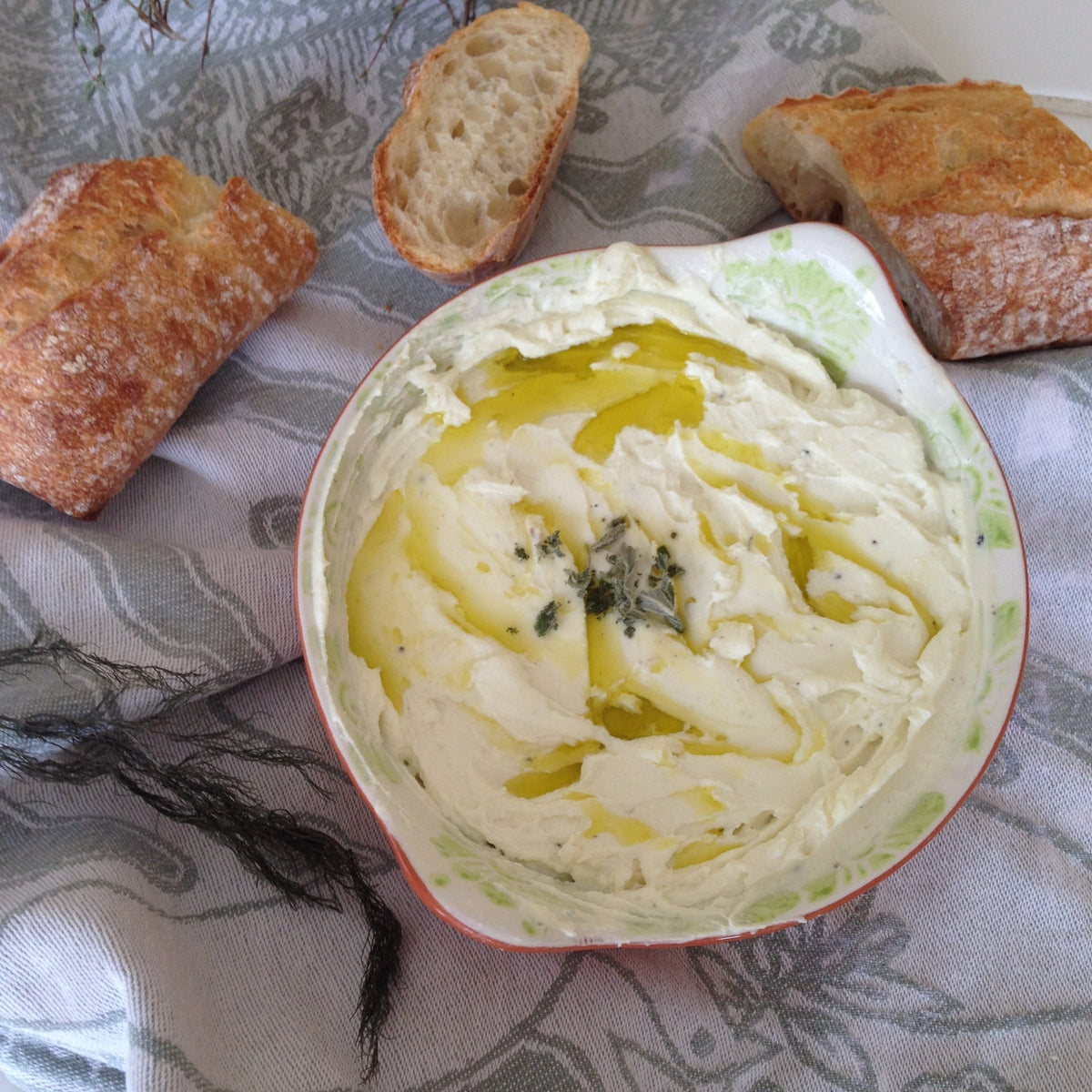 Creamy whipped cheese spread drizzled with olive oil and garnished with herbs, served with slices of crusty artisan bread for dipping and spreading.