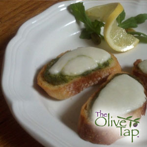 Baguette slices topped with pesto and mozzarella cheese, garnished with a twisted lemon slice and greens.