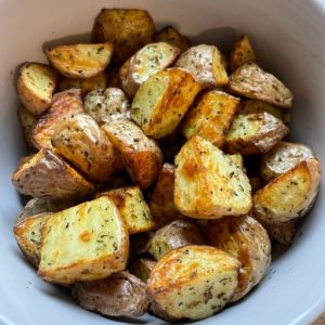 Roasted rosemary potatoes with crispy golden-brown edges and herb seasoning, served in a white bowl.