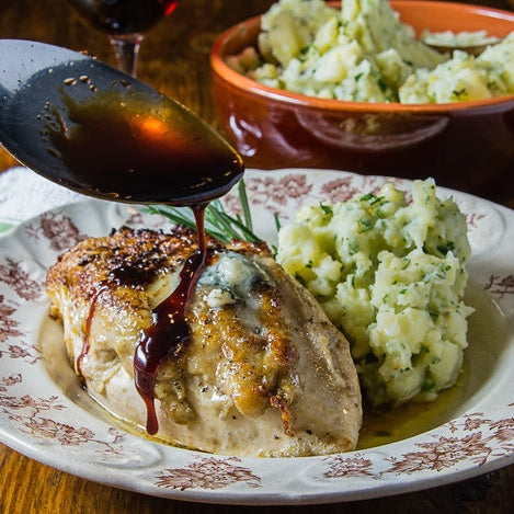 Stuffed chicken breast topped with a gastrique sauce, served alongside creamy herb mashed potatoes on a decorative white plate.