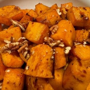A close-up of roasted, diced sweet potatoes topped with chopped walnuts.