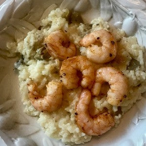 Creamy parmesan risotto with mushrooms topped with sauteed shrimp and served in a decorative white bowl.