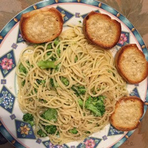 Plate of spaghetti tossed with broccoli florets and garlic, served with toasted crostini slices on the side.