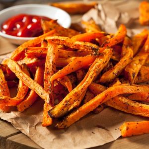 Seasoned, crispy sweet potato fries, served on parchment paper with a side of ketchup.