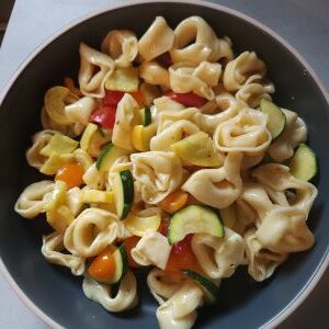 Tortellini pasta with sliced zucchini and cherry tomatoes, served in a dark-colored bowl.