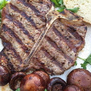 grilled T-bone steak with bold charred grill marks, served with roasted mushrooms, crusty artisan bread, and garnished with fresh parsley.