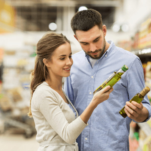 A man and woman in a grocery store examining bottles of olive oil and reading product labels.