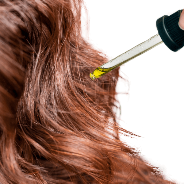 A dropper applying olive oil to brown hair as part of a hair care treatment.