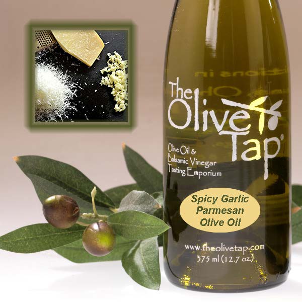 Bottle of Spicy Garlic Parmesan Olive Oil from The Olive Tap next to olives and leaves with an inset showing grated parmesan, a block of parmesan, and garlic on a light background.