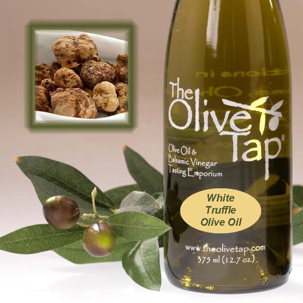 A bottle of White Truffle Olive Oil from The Olive Tap next to olives and leaves with an inset showing fresh truffles on a light background.