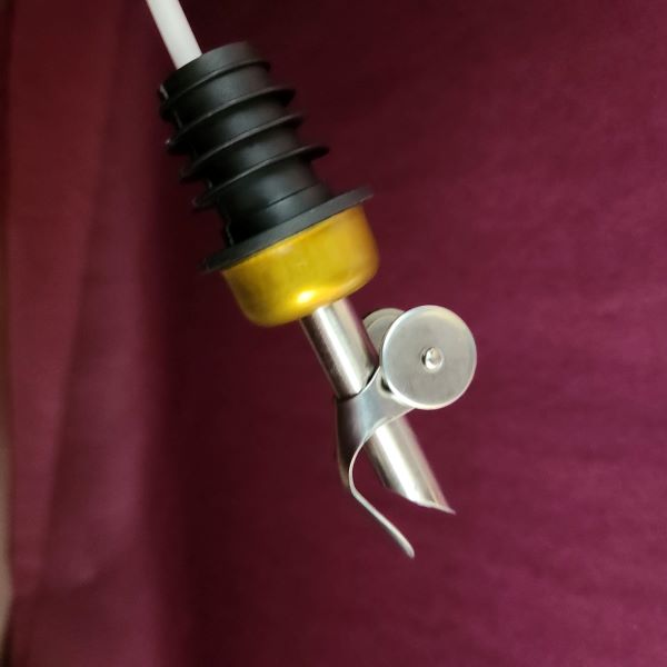 Olive oil pour spout with a yellow cap and black rubber sleeve on a maroon background.