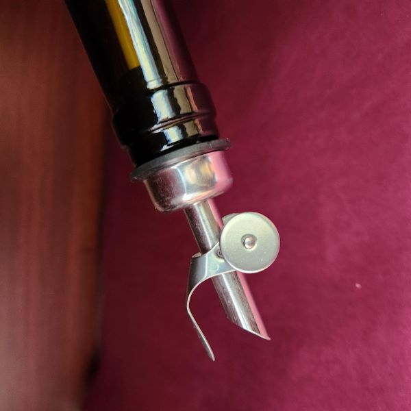 Silver olive oil pour spout in the opening of a glass bottle in front of a maroon background.