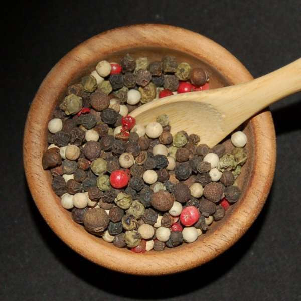 5 Peppercorn Blend In Jar from The Olive Tap: A blend of red, brown, green, black, and white peppercorns in a wooden bowl with a wooden spoon in it against a black background.