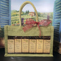 You Pick 6 Sampler Set from The Olive Tap: Six bottles of olive oils and vinegars in a green canvas gift bag with handles and a bow in front of a countryside mural.