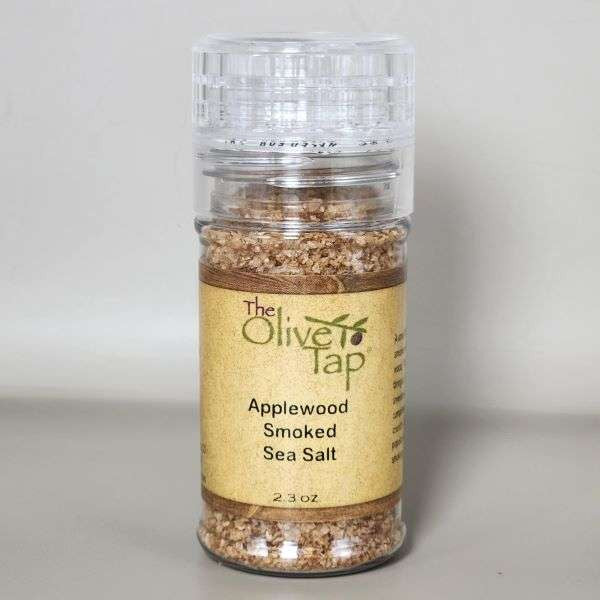 Applewood Smoked Sea Salt in a grinder jar from The Olive Tap with The Olive Tap logo and olive branch against a neutral background.
