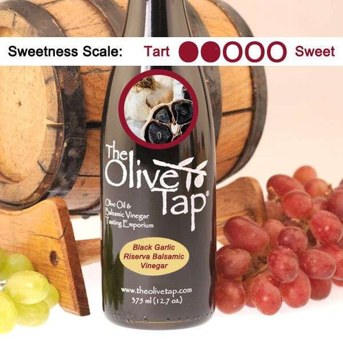 A bottle of Black Garlic Riserva Balsamic Vinegar with a picture of fresh black garlic, surrounded by grapes in front of a wooden barrel, and a sweetness scale indicating a two on a light background.