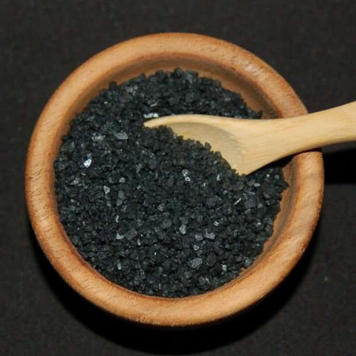 Black Hawaiian Sea Salt from The Olive Tap: Black pebble-sized pieces of sea salt in a wooden bowl and a wooden spoon against a black background.