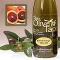 A bottle of Blood Orange Olive Oil from The Olive Tap next to olives and leaves with an inset showing a sliced blood orange on a light background.