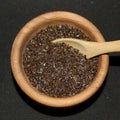 Campfire Smoked Sea Salt from The Olive Tap: Brown grains of sea salt in a wooden bowl and a wooden spoon against a black background.