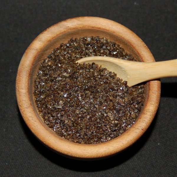 Campfire Smoked Sea Salt from The Olive Tap: Brown grains of sea salt in a wooden bowl and a wooden spoon against a black background.