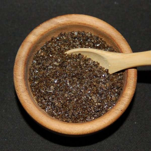 Campfire Smoked Sea Salt from The Olive Tap: Brown grains of sea salt in a wooden bowl and a wooden spoon against a black background.