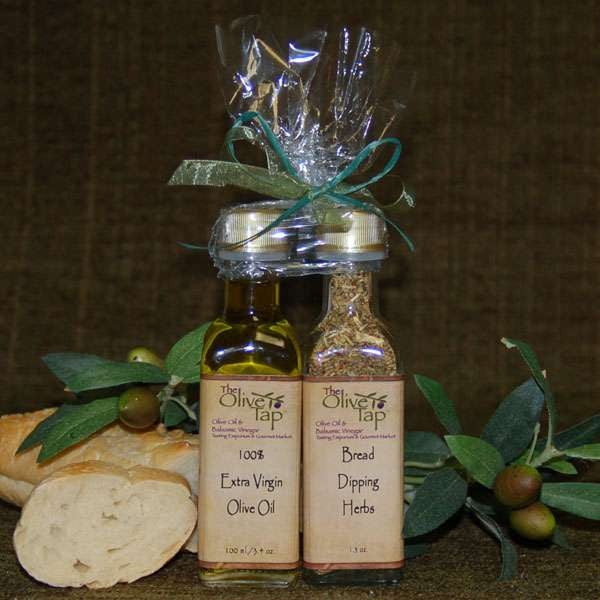 Bread Dipping Pairing Set with Standard Trim from The Olive Tap: A bottle of olive oil and a bottle of bread dipping herbs tied with a bow next to bread and olives and leaves on a brown background.