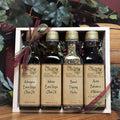 The Bread Dipping Sampler from The Olive Tap: Two bottles of olive oil, one bottle of bread dipping herbs, and one bottle of balsamic vinegar inside of a wooden box with a bow and grapes, leaves, and a wooden barrel in the background.