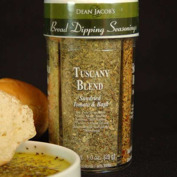 4-Variety Bread Dipping Seasonings Large Size from The Olive Tap next to a bread dipping plate with olive oil and seasoning in it with fresh sliced bread against a black background.