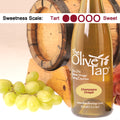 Bottle of The Olive Tap Champagne Vinegar with grapes and a wooden barrel in the background